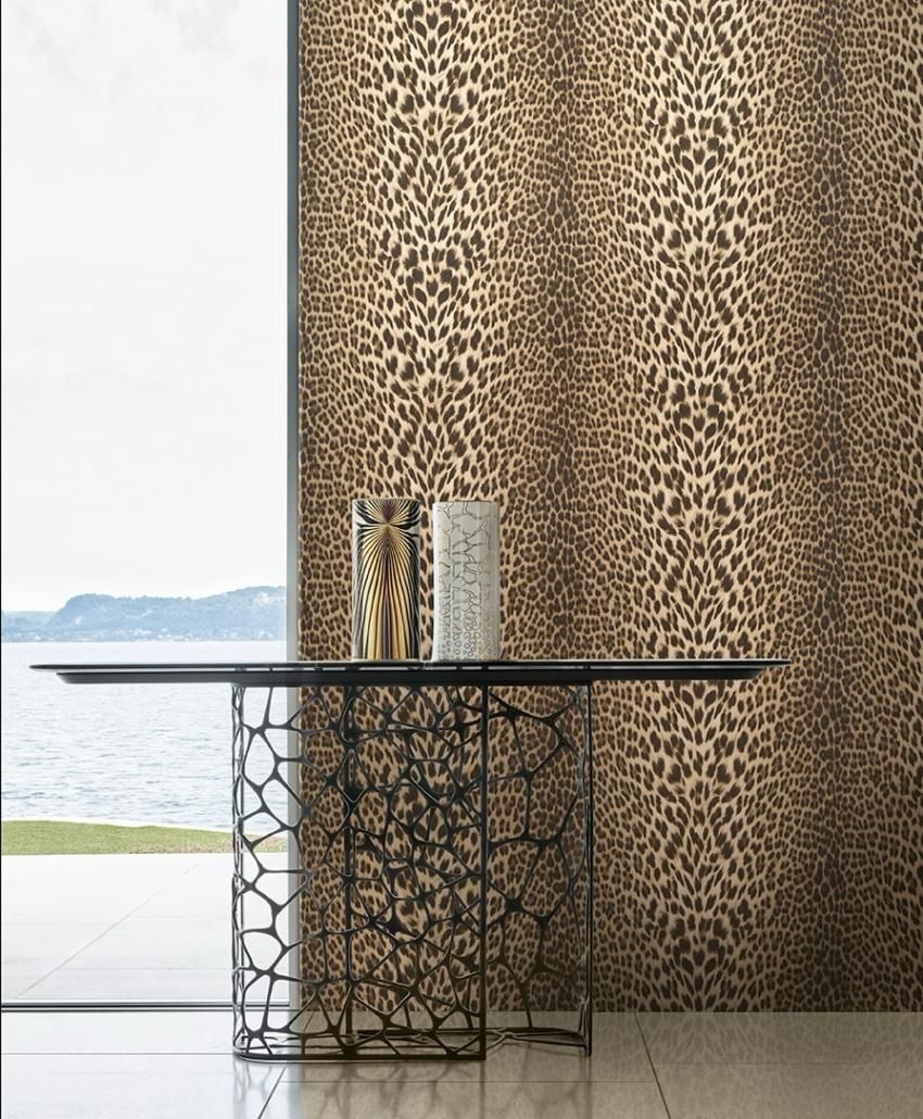 Una stanza con un tavolo con gambe dorate e una sedia tigrata su uno sfondo di carta da parati con motivi verdi e beige.