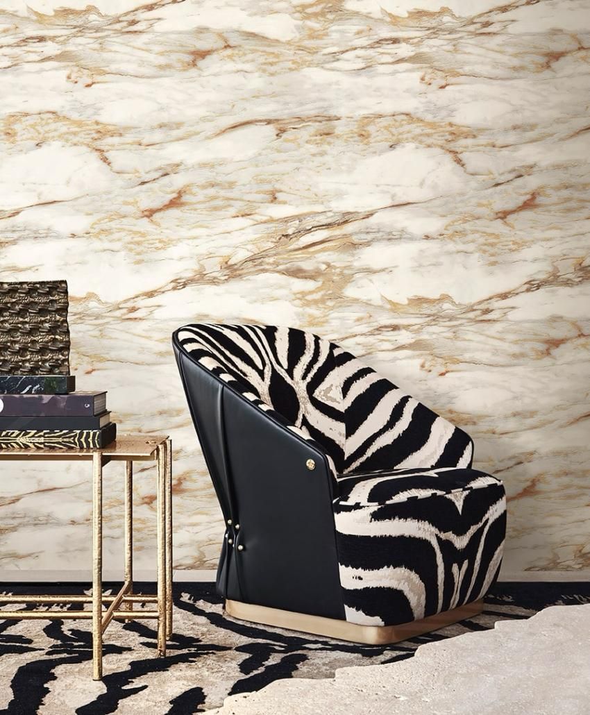 Poltrona con stampa zebrata, schienale in pelle nera, tavolino dorato con libri, parete in marmo, tappeto con stampa zebrata.
