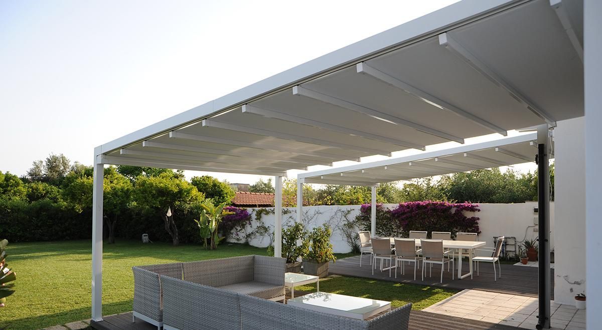 Pergola bianca sopra un patio con posti a sedere all'aperto, prato e verde.