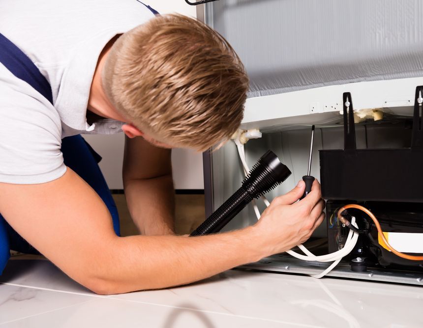 A Man Is Working On A Refrigerator With A Flashlight — South Coast Refrigeration & Air Conditioning In Bomaderry, NSW
