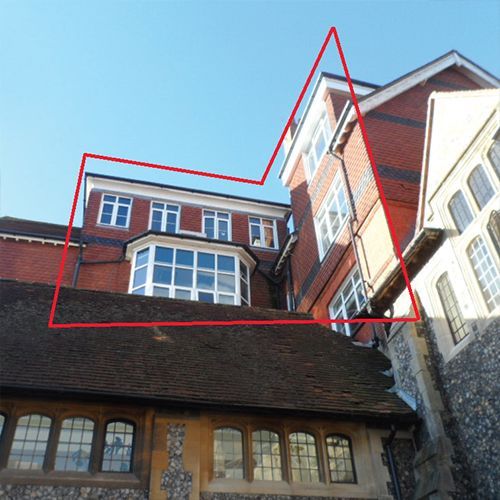 Red-brick building with multiple windows, dark roof, and a bright blue sky.