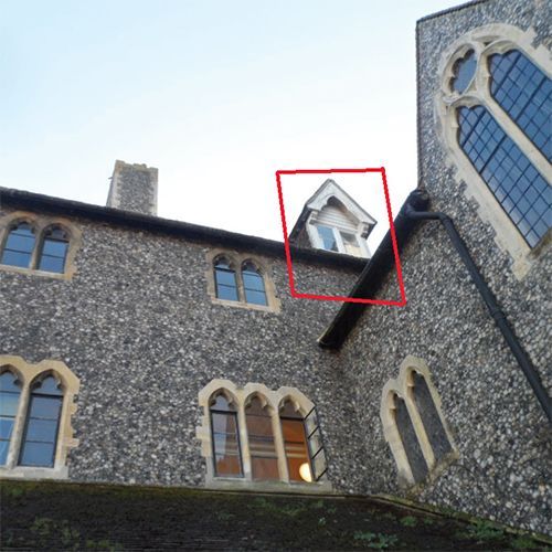 Red box highlights a small window on a stone building's roof. The building has several arched windows.