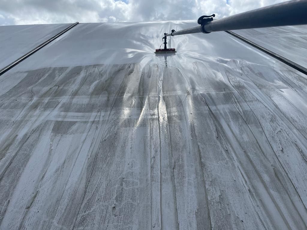 Cleaning a large white tarp roof with a long-handled brush and water.
