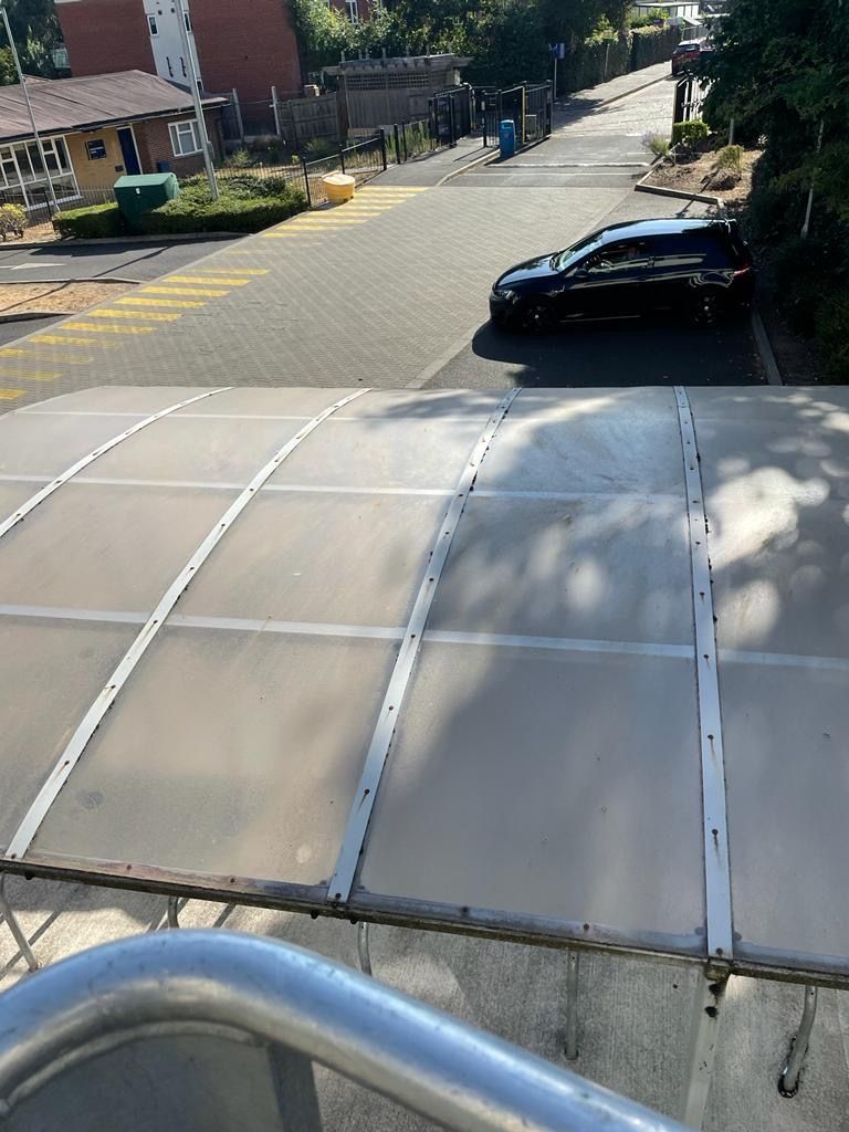 Overhead view of a street with a black car parked, a walkway with a transparent roof, and buildings.