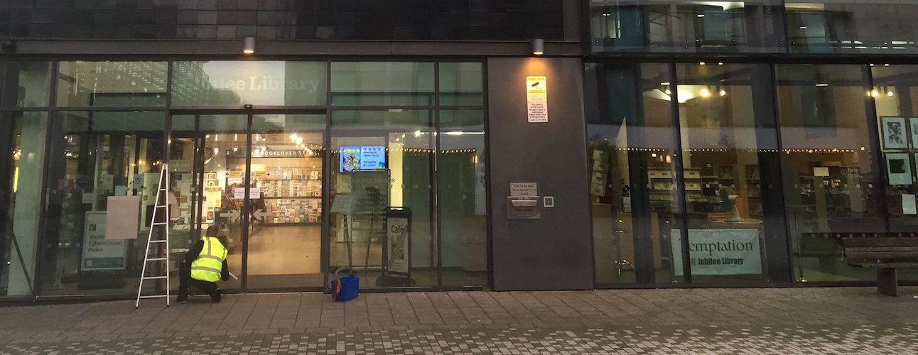 Demonstrating what is Commercial window cleaning, shop front glass being cleaned professionaly by hand in the early morning hours.