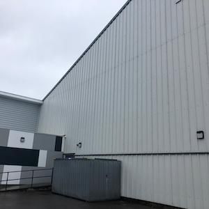 Exterior of a building with corrugated white metal siding. A gray storage container sits in front. Overcast sky.