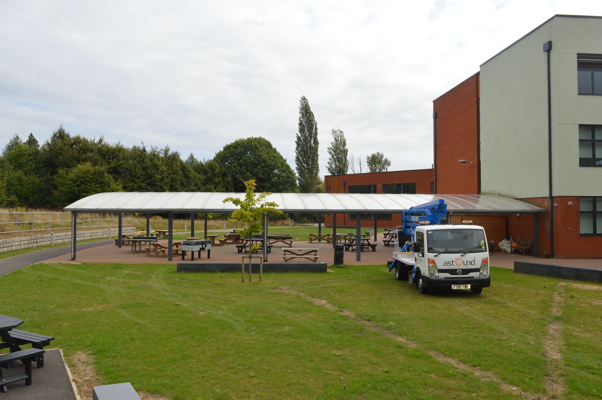 Schoolyard with canopy, tables, truck, green grass, and brick and white building.