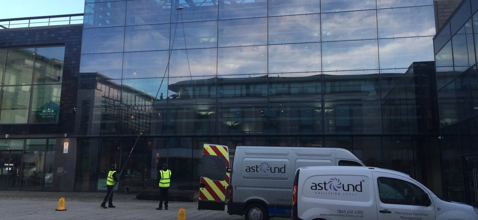 Astound Cleaning Group branded vans at a modern commercial glass-façade building — professional commercial window cleaning Sussex & South London