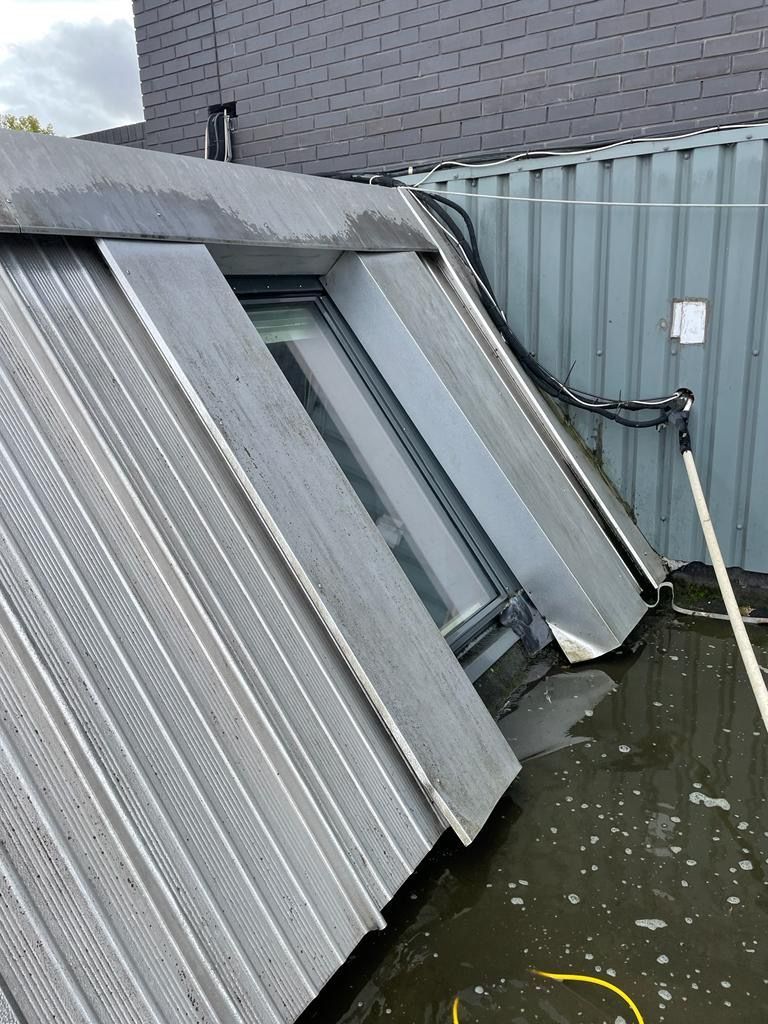 Angled roof with a window, water pooling around it. Grey corrugated metal panels, black tubing.