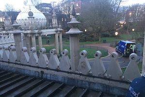Ornamental balcony with ornate columns and Brighton Pavilion in the background; a police vehicle is in the park.