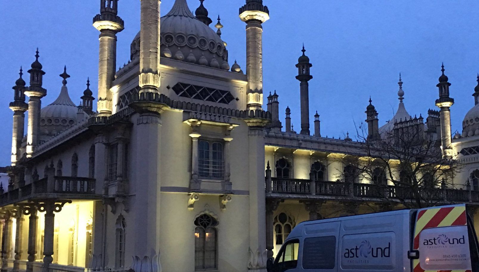 Brighton Pavilion illuminated at dusk, with a service van in the foreground.