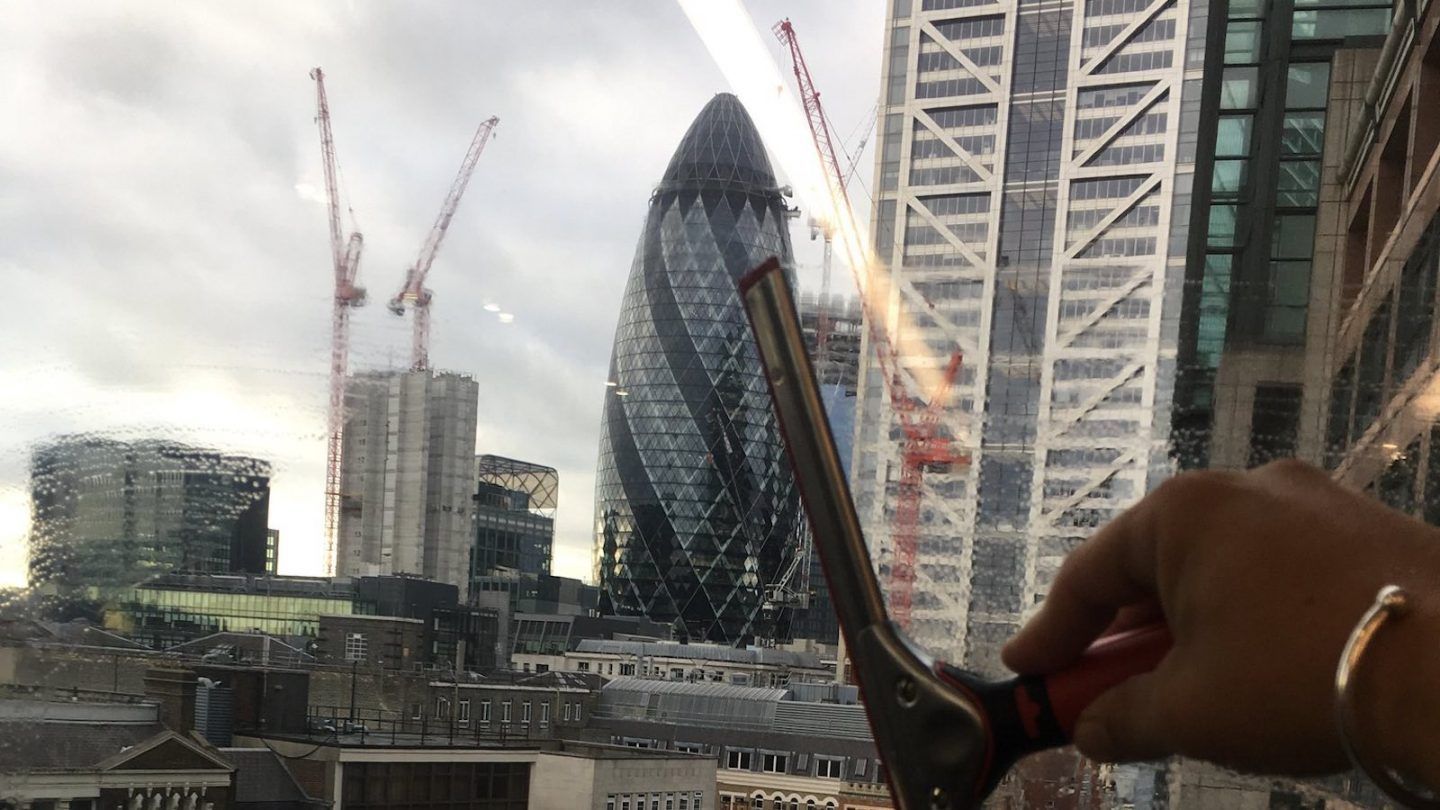 Man cleaning inside of windows looking out over london skyline