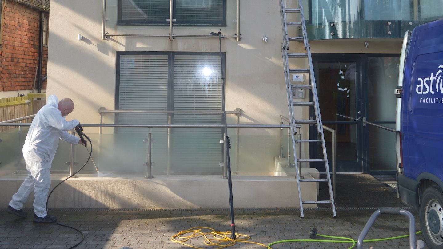 Astound operator pressure washing the outside of a home with astound van to the right of image