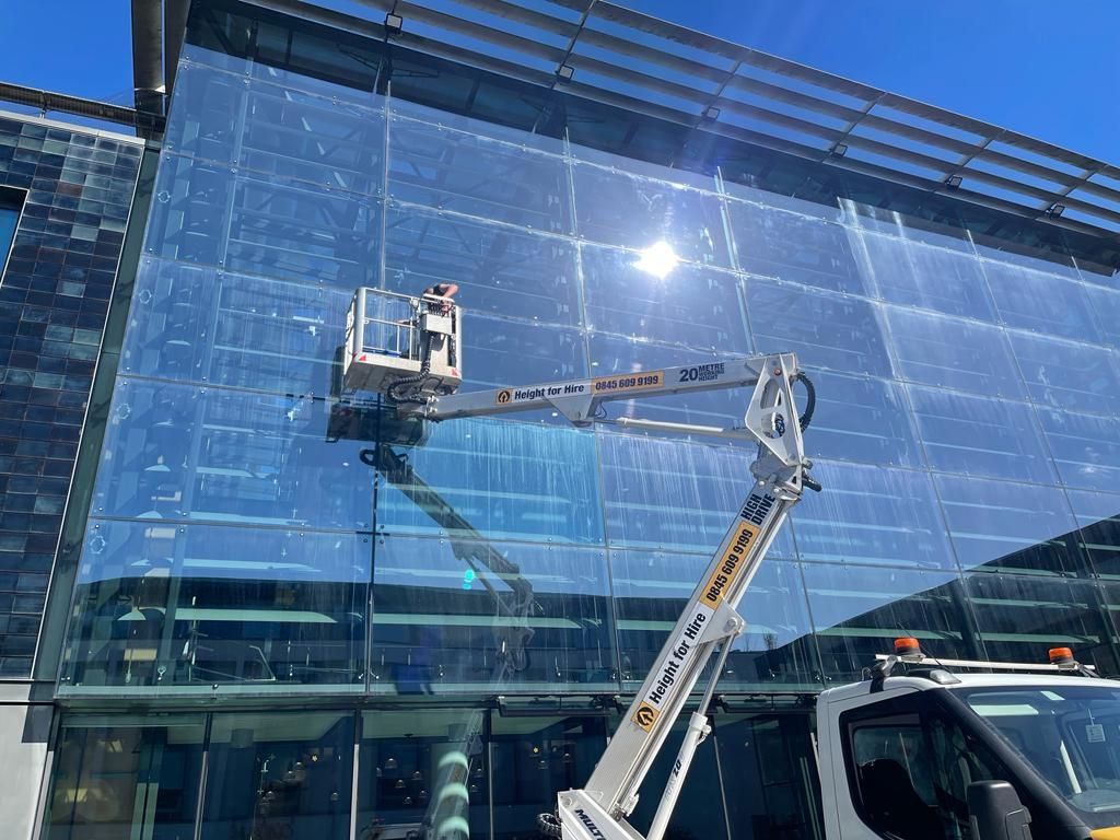 Glass building with a cherry picker in foreground demonstrating What Is Commercial Window Cleaning