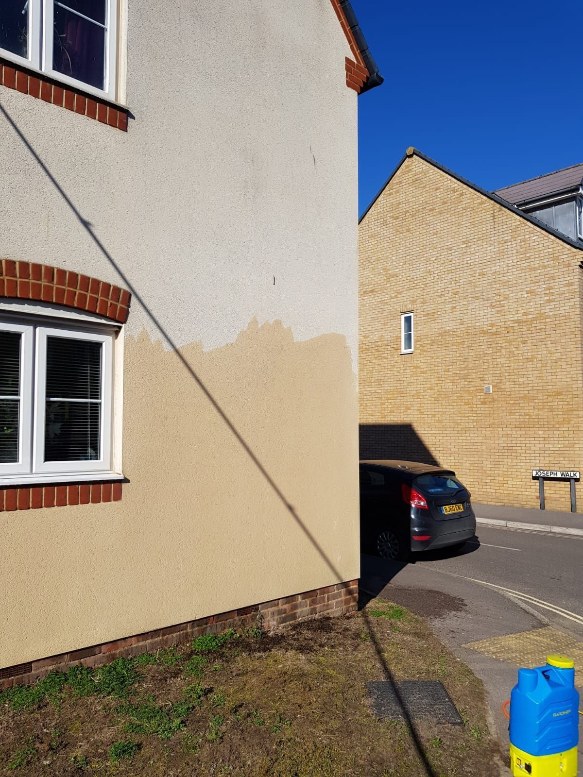 Side of a building, faded stucco. Car parked beside the building, blue sky.