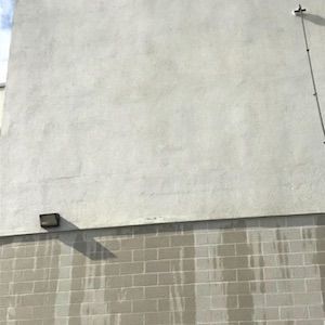 Gray concrete block wall with a light, water stains, and a utility line.