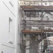 White building next to scaffolding at a construction site, showing exposed brickwork.