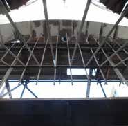 Interior view of a damaged roof structure, showing beams, missing sections, and sunlight.