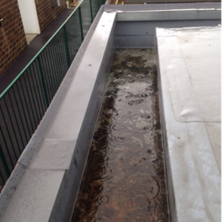 A drain on a roof with a green fence in the background