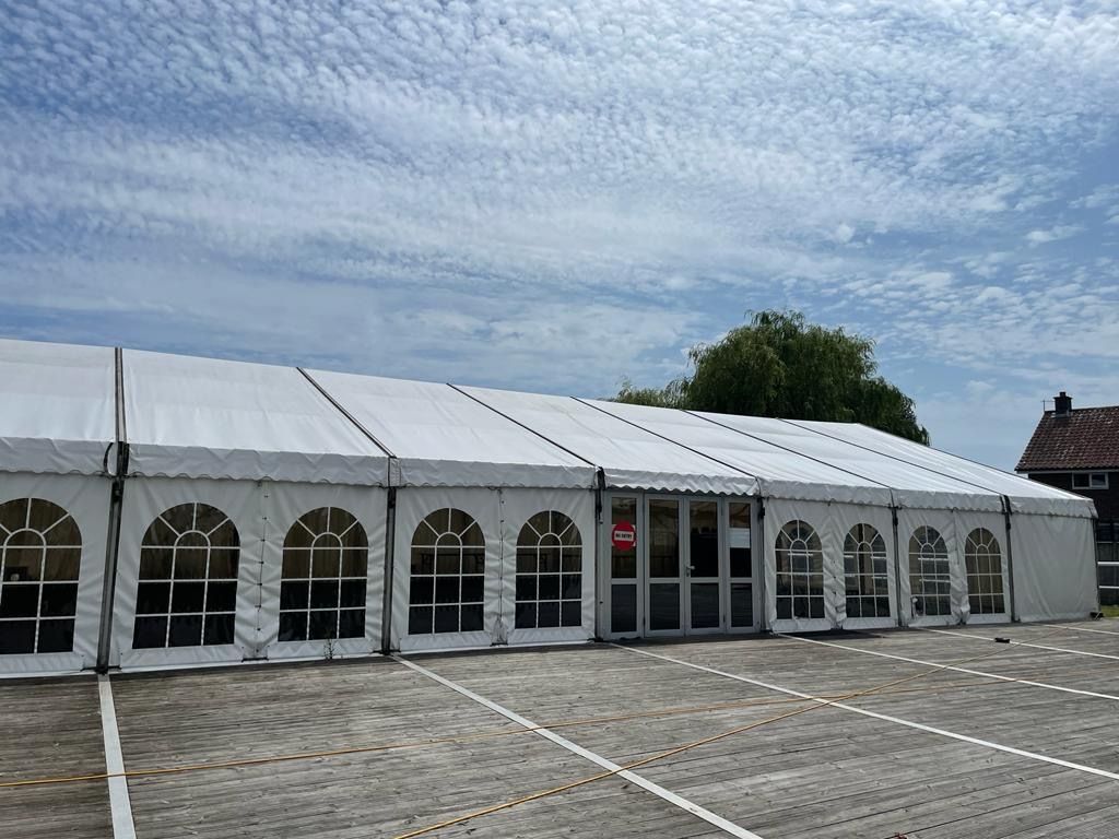 Large white tent with arched windows and a glass door on a paved lot under a cloudy sky.