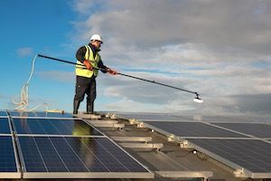 A man is cleaning solar panels on the roof of a building.