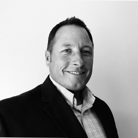 Smiling man in a suit jacket and collared shirt against a white background.