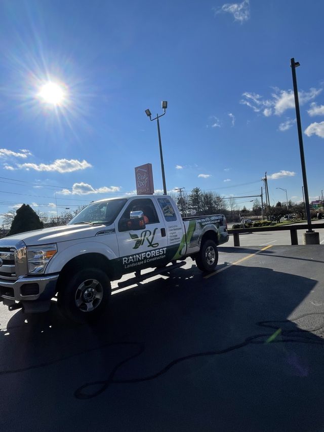 A white truck with the Rainforest Landscape logo is parked in a parking lot on a sunny day.