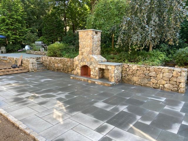 A patio with a stone fireplace and a stone retaining wall.