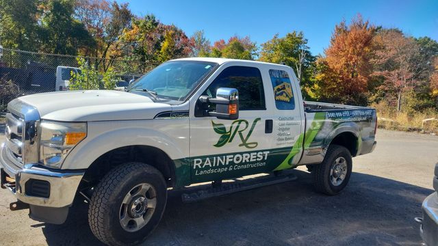 A white truck with the Rainforest Landscape logo on the side is parked in a parking lot.