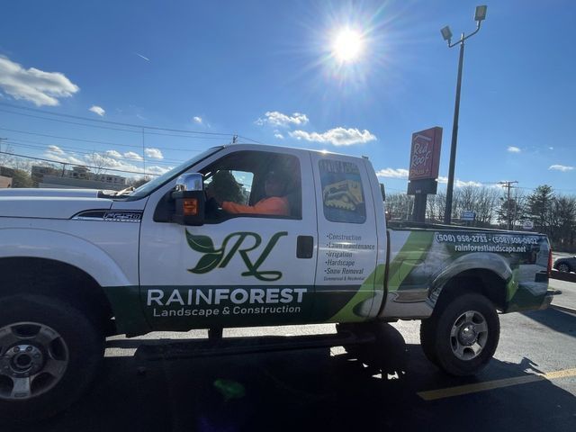 A white truck with the logo for Rainforest Landscape a landscaping & excavation company is parked in a parking lot