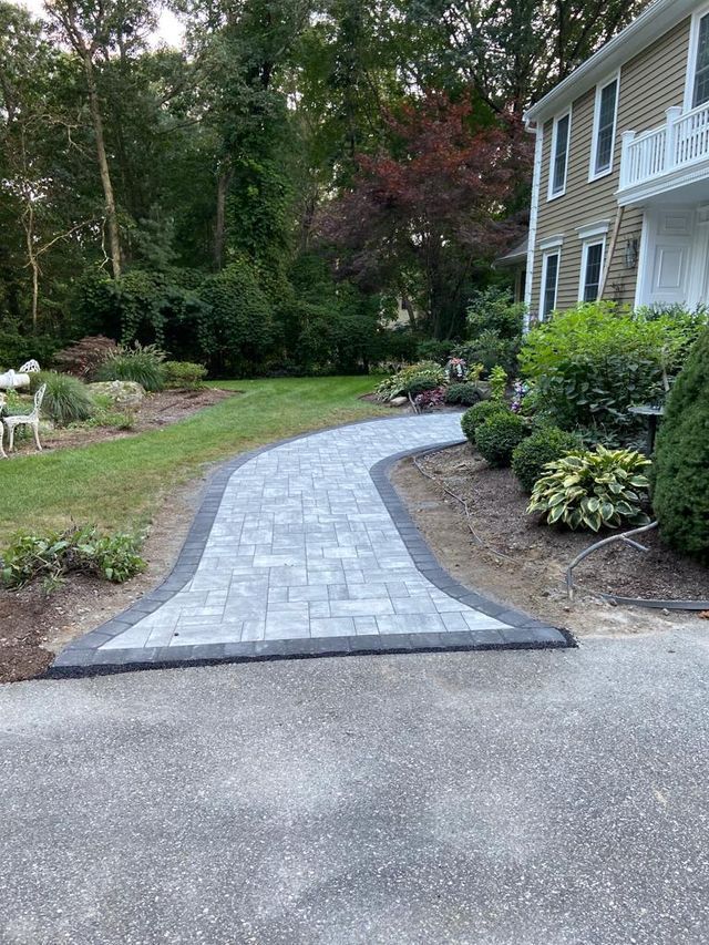 A brick walkway leading to a house in a backyard.