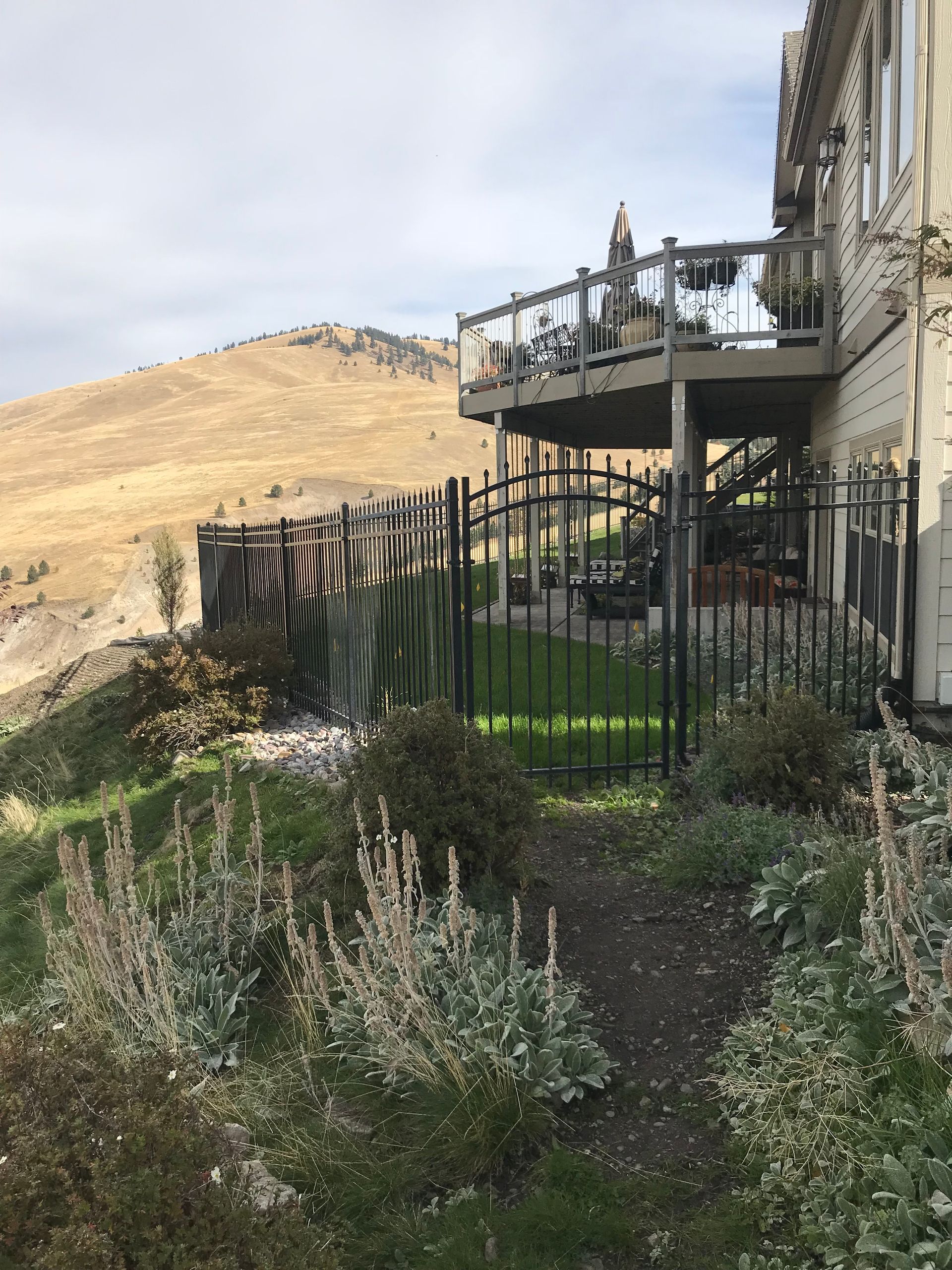 Black fenced yard with gate leading to a deck, with a hilly background.