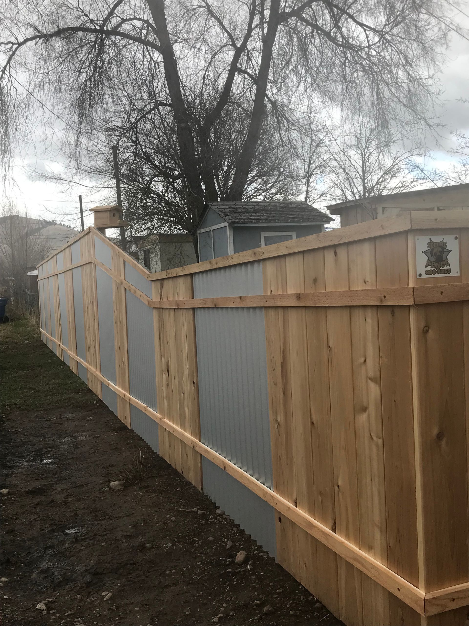 Wooden fence with corrugated metal panels; cloudy day.