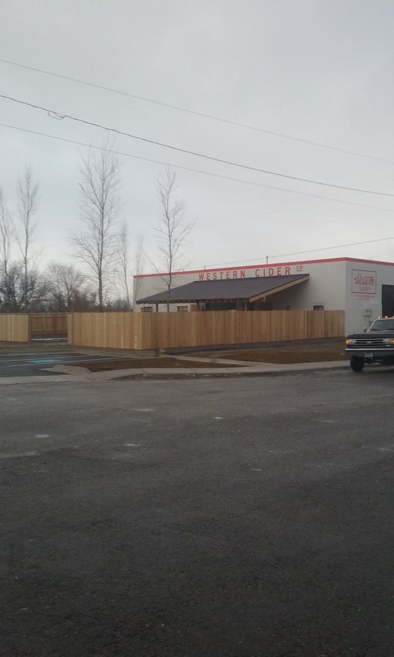 A building with a wooden fence in front. A cloudy day, empty parking lot.