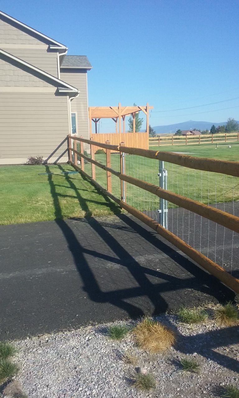 Wooden fence with wire mesh runs alongside a house on a sunny day.
