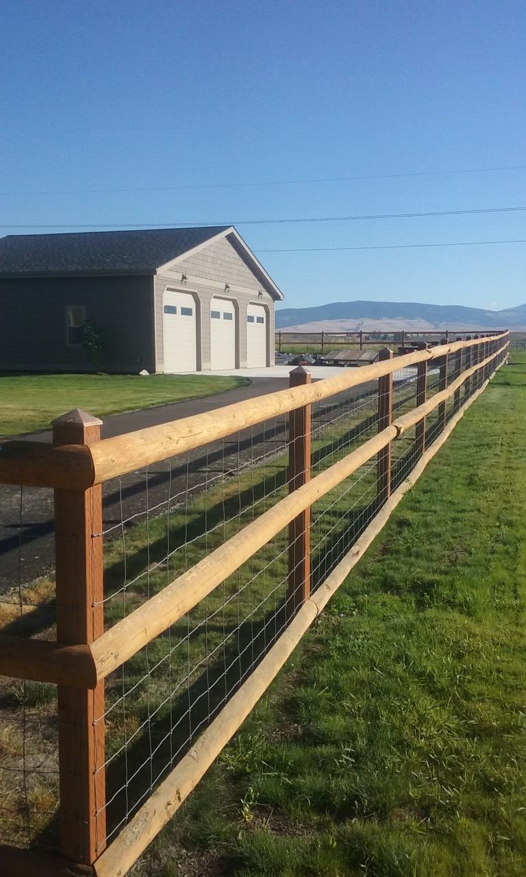 Wooden fence with wire mesh, alongside a driveway, leading to a garage under a blue sky.