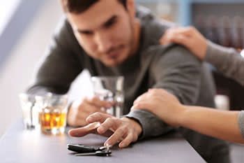 a man is sitting at a table with a glass of whiskey and a car key .