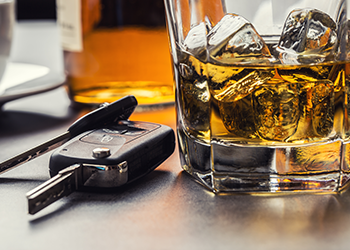 a glass of whiskey with ice cubes and a car key on a table .