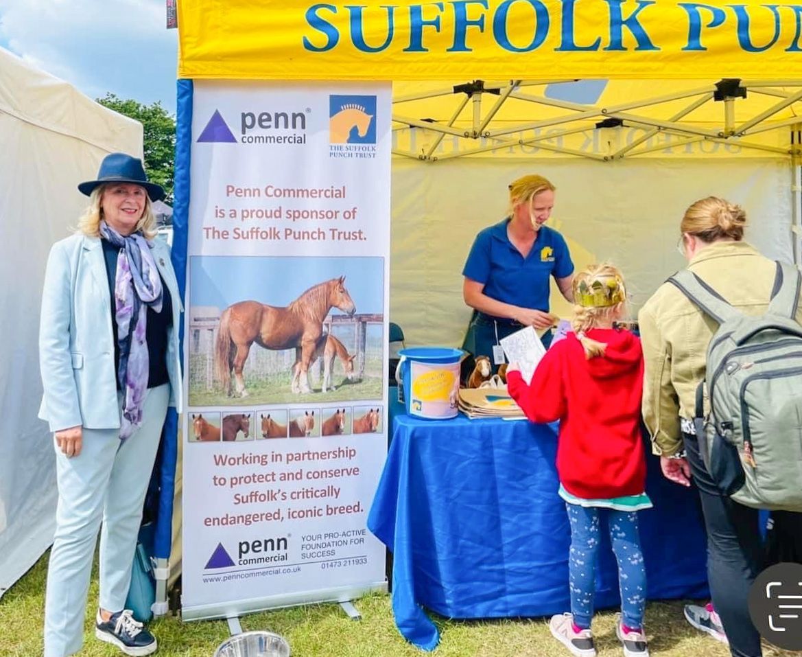 a woman is standing in front of a sign that says Suffolk Punch Trust, raising money for the charity