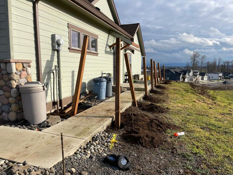 Construction of a fence beside a house with wooden posts and a concrete walkway.