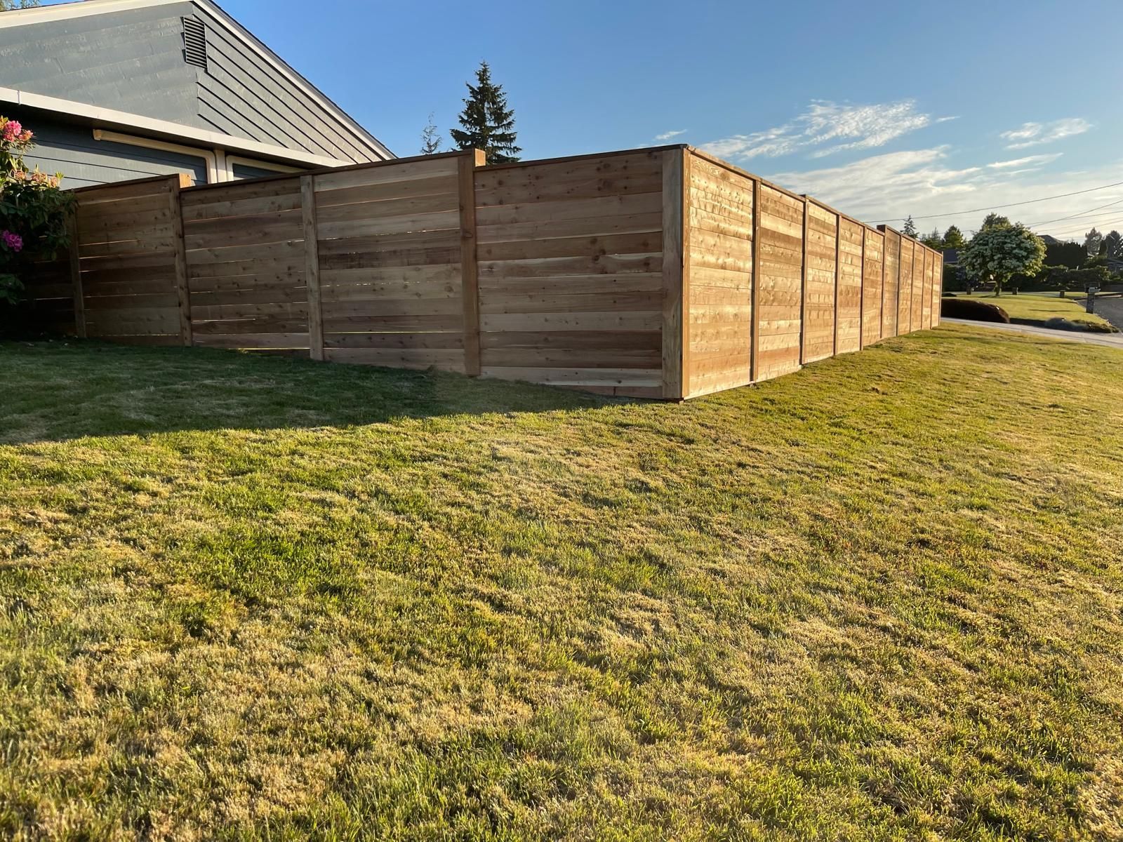 Wooden fence surrounding a grassy yard under a blue sky.