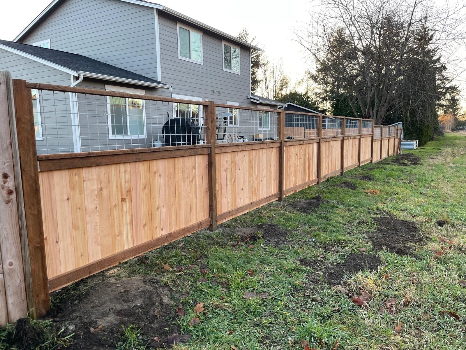 Wooden fence enclosing a grassy yard next to a two-story house.