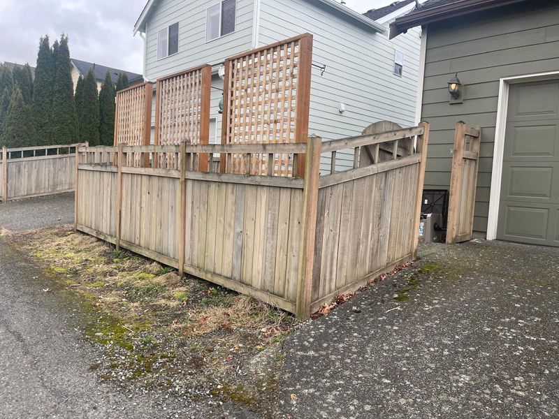 Wooden fence with lattice panels, bordering a gravel driveway and a house with a garage.