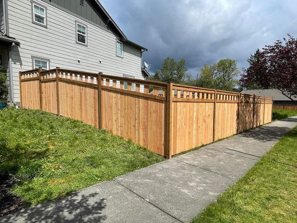 Wooden fence bordering a grassy yard and a sidewalk, under a cloudy sky.