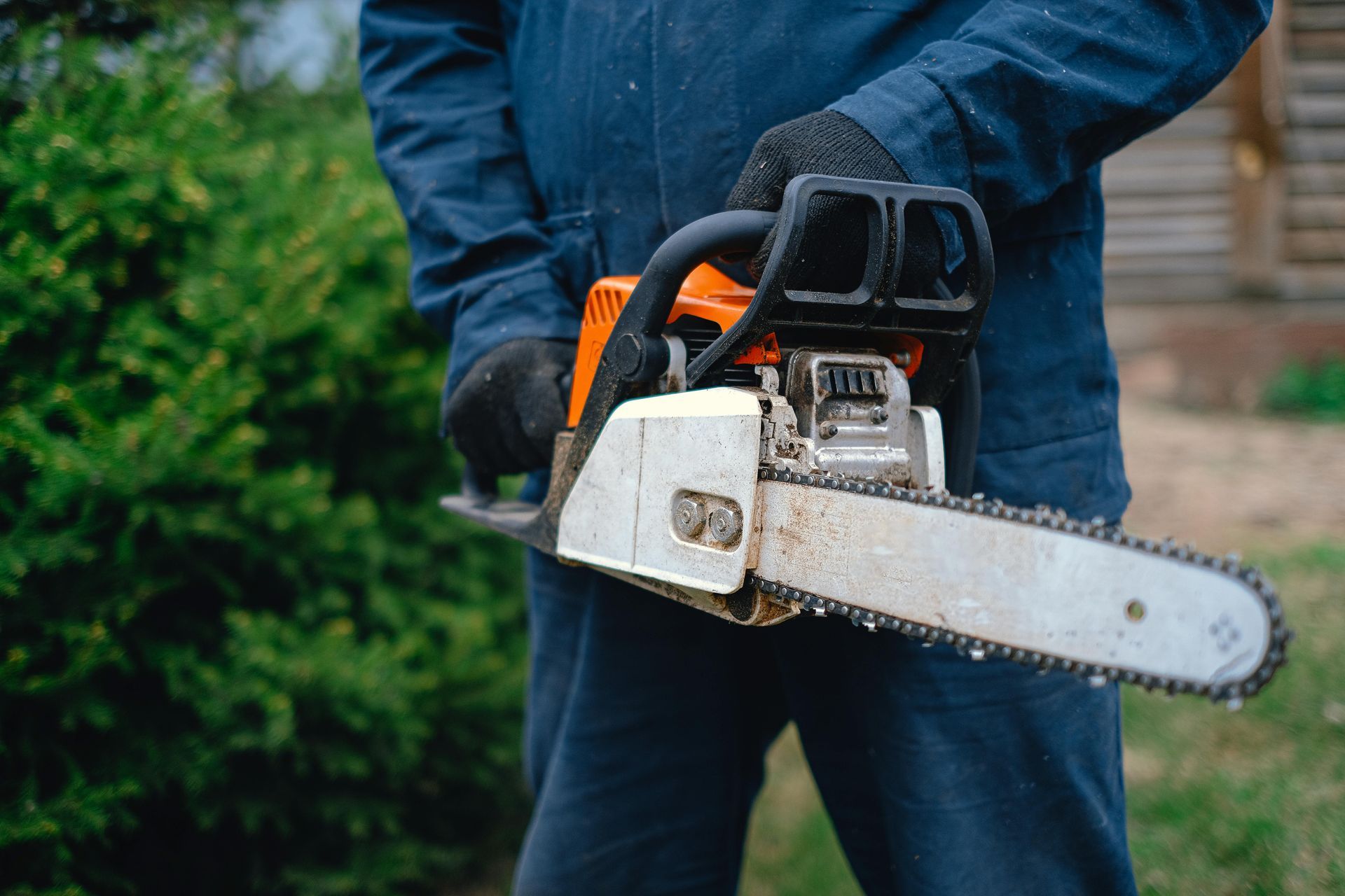 Person in blue overalls holding an active chainsaw outdoors.