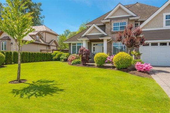 Two-story house with green lawn, driveway, and colorful landscaping under a bright blue sky.