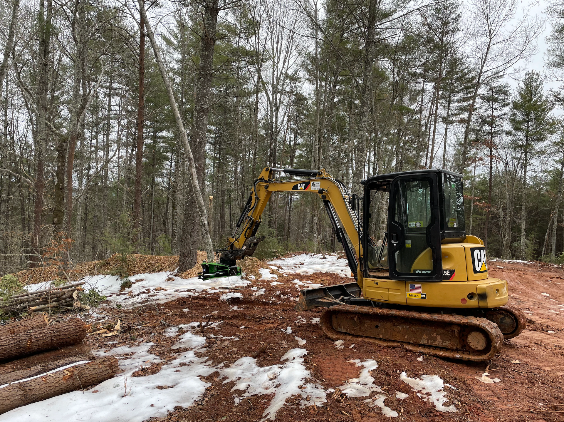 A yellow excavator is sitting in the middle of a snowy forest.