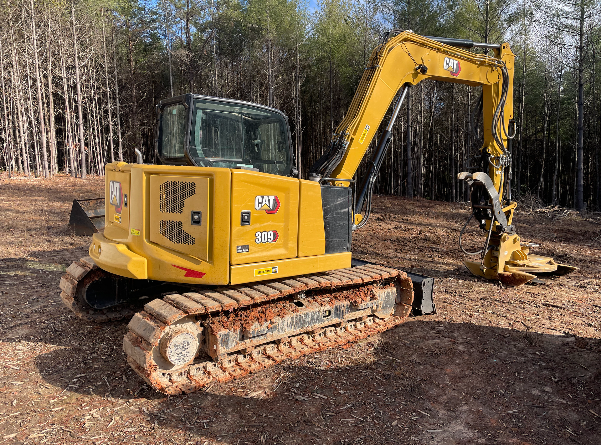 A yellow excavator is parked in a dirt field in front of a forest.