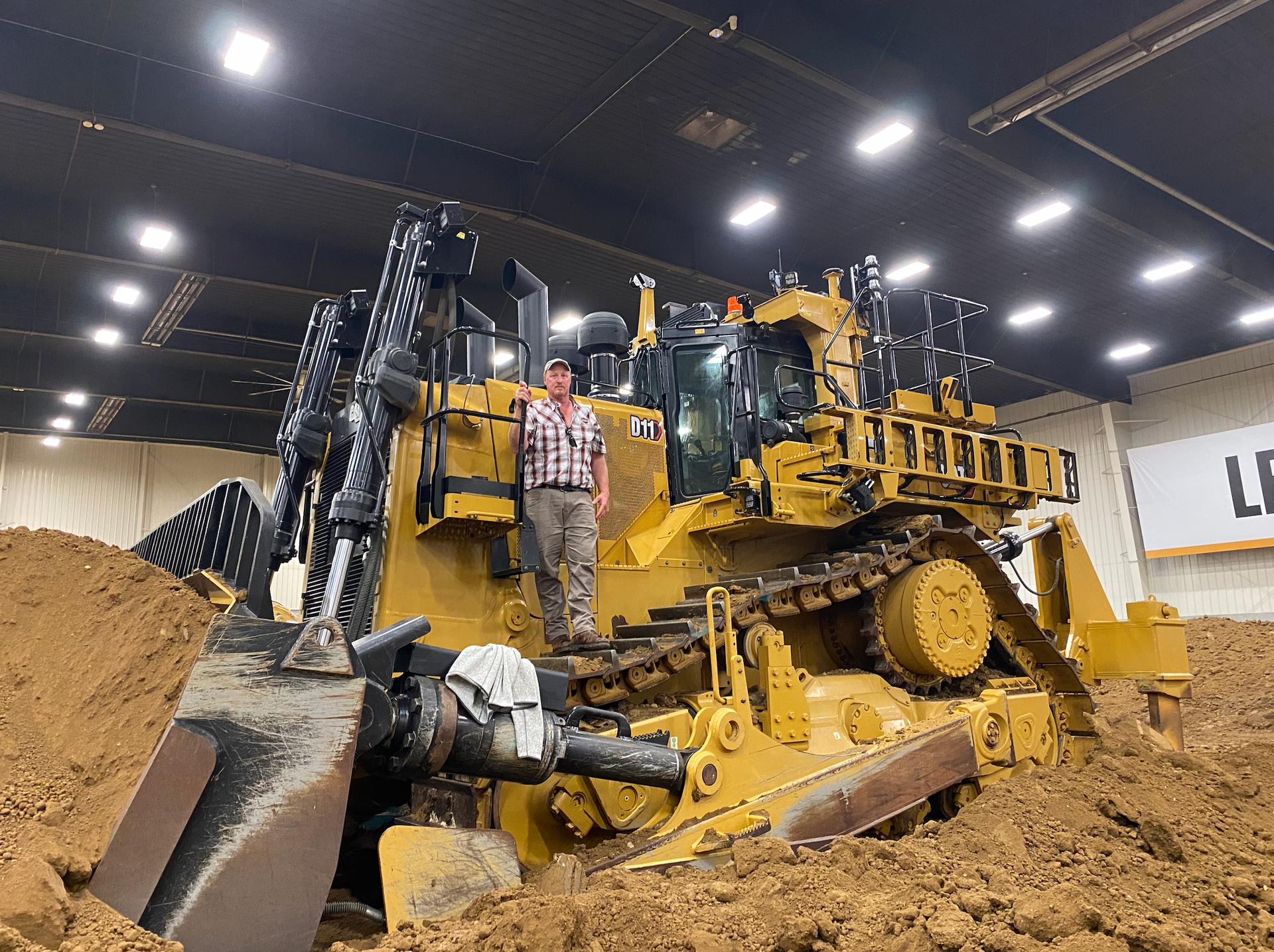 A man is standing next to a large bulldozer in a building.