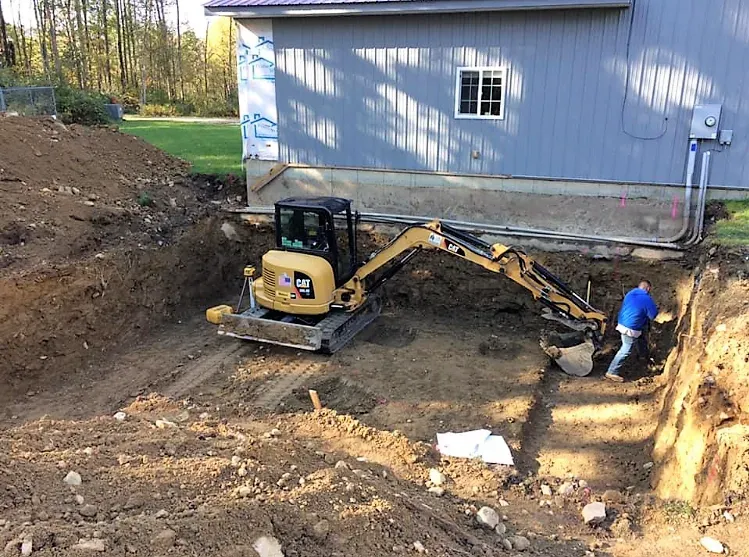 A man is digging a hole with an excavator in front of a house.